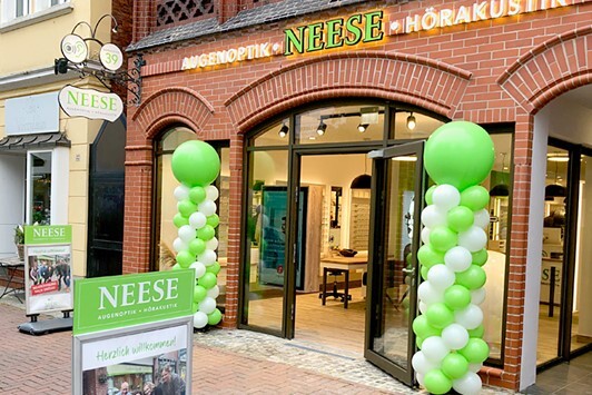 Das Ladengeschäft von Neese Augenoptik und Hörakustik mit grüner Dekoration am Eingang.