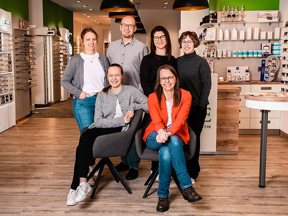 Teamfoto in Optiker-Fachgeschäft mit Brillenregalen und Beratungstresen.
